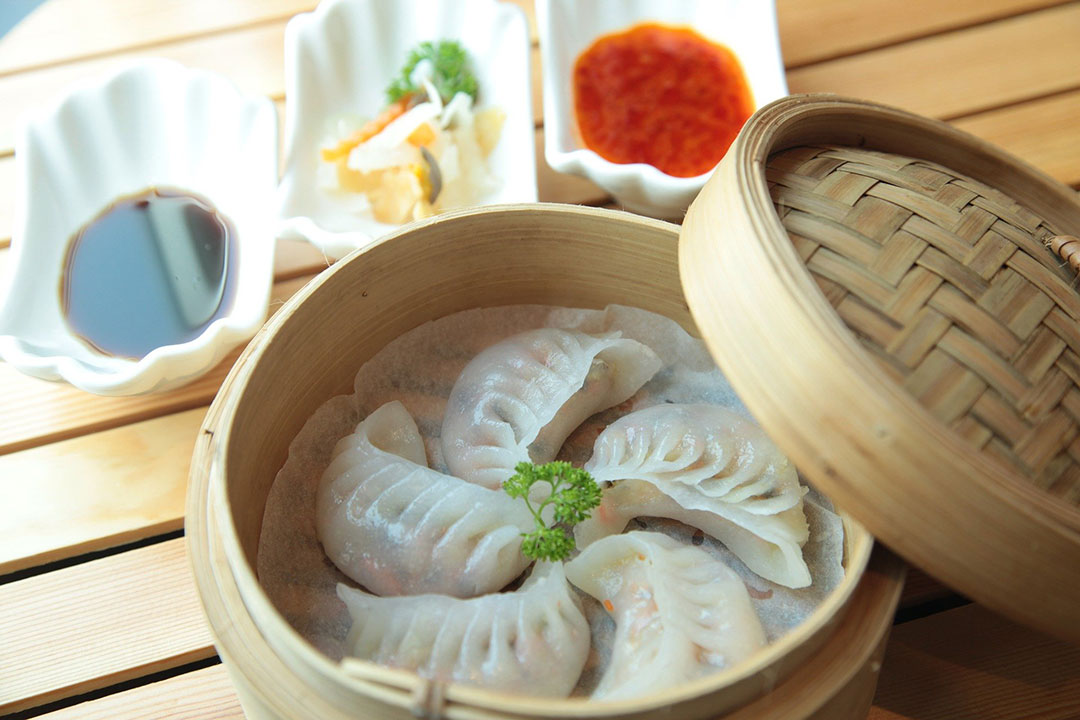 dumplings in a wooden basket with sauce on the side